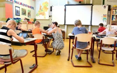 Lehrperson kniet bei Schüler*in in Klassenzimmer