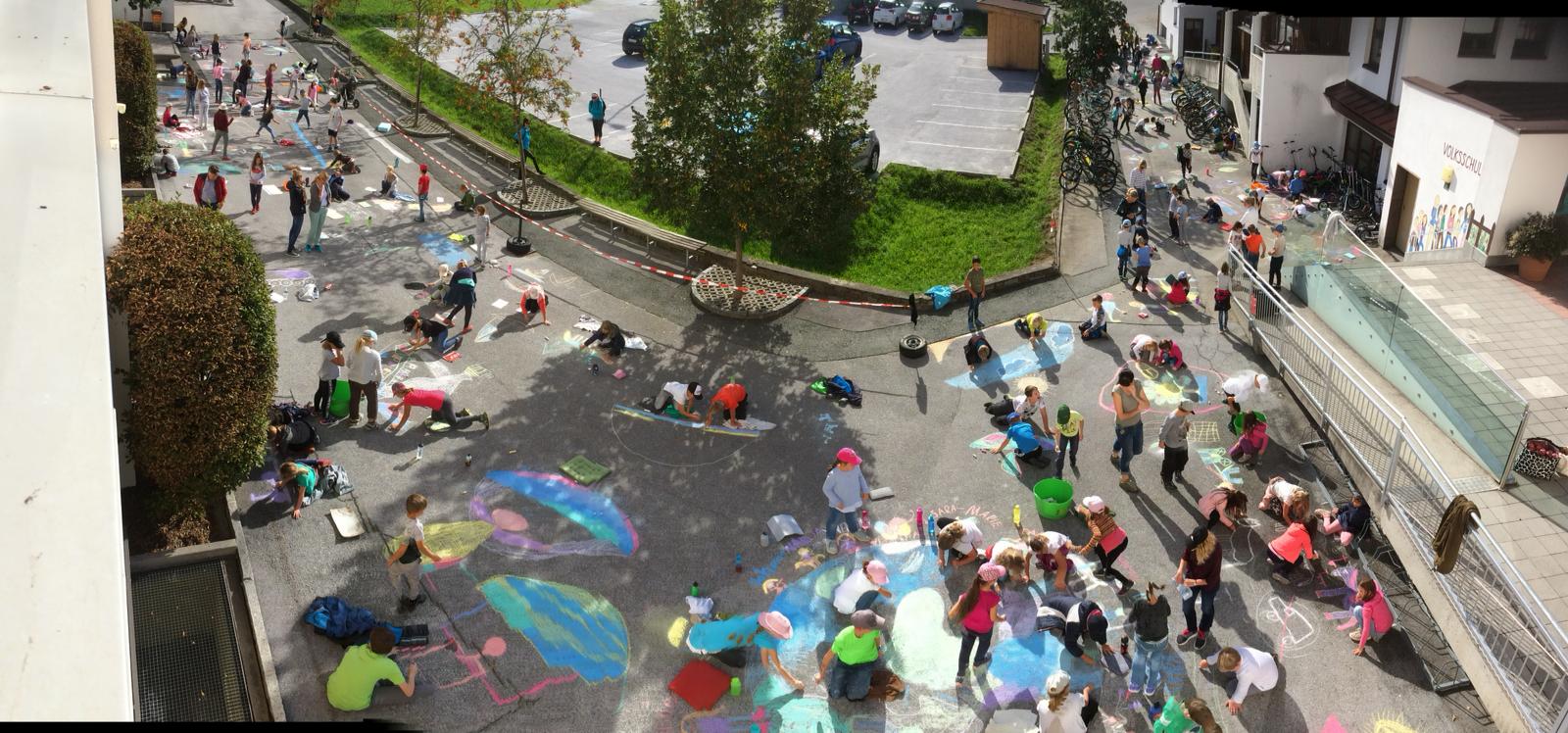 Aus der Vogelperspektive sieht man, wie junge Menschen mit Kreide große Bilder auf der Straße gestalten.