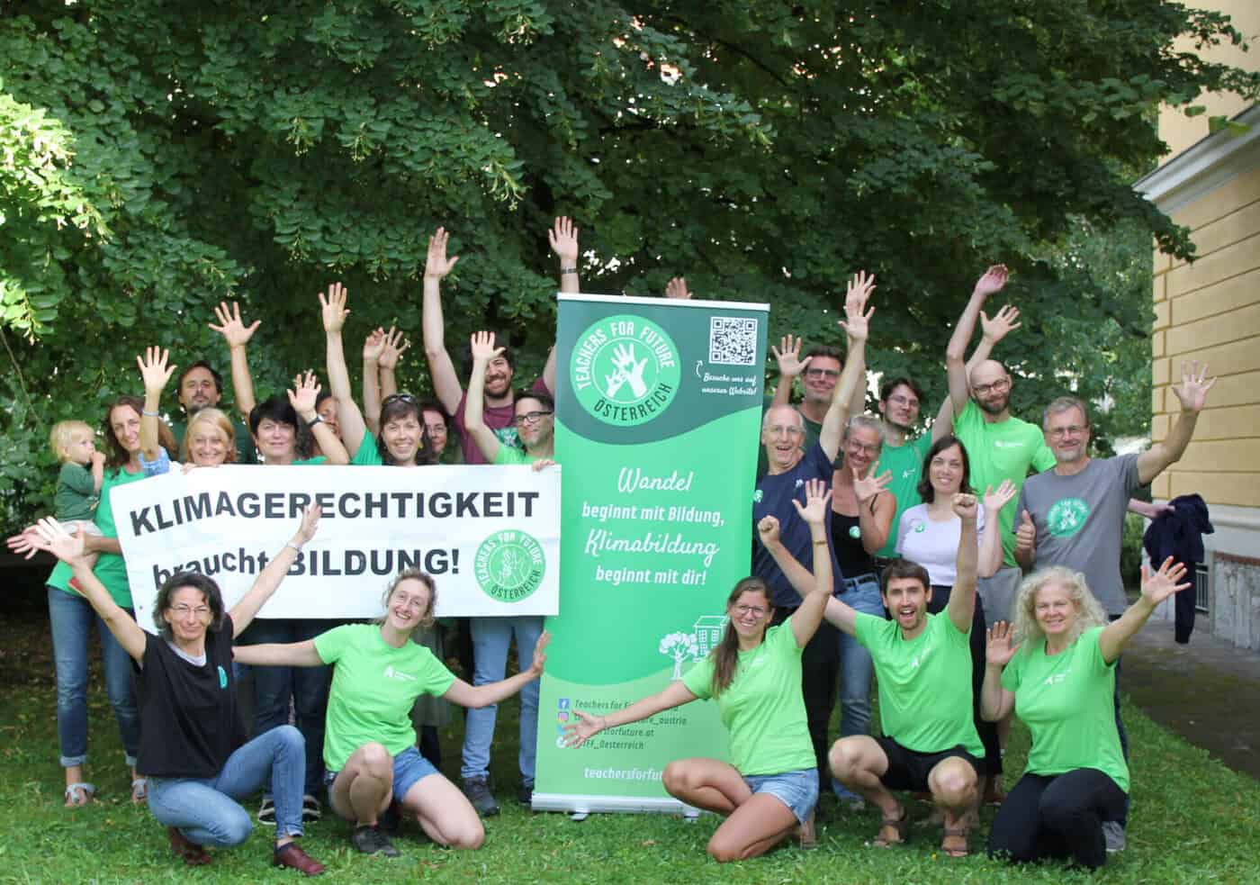 Teachers For Future Österreich jubeln. Auf einem Rollup-Banner in der Mitte steht unter dem TFF-Logo: "Wandel beginnt mit Bildung, Klimabildung beginnt mit dir!"